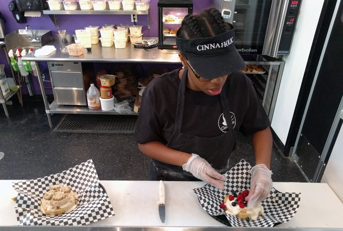 An associate sprinkles fresh berries on a frosted bun.